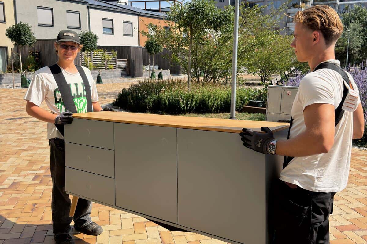 Två från Rutly bär en byrå mellan sig utomhus